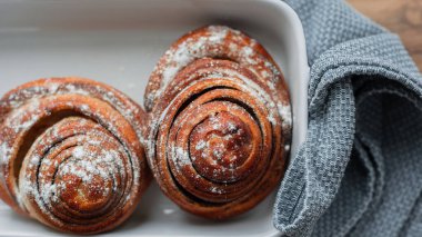 Taze çörekler seramik tepside uzanıyor, mutfak havlularıyla, üst manzara. Tatlı un ürünleri fırını. Ev yapımı.