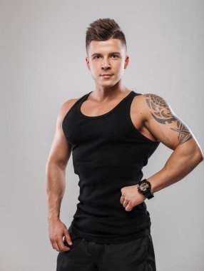 Stüdyo erkek portresi. Yakışıklı, güçlü, atletik erkek modeli. Sağlıklı, siyah atlet gömlekli, gri arka planda poz veriyor.