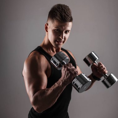 Güçlü yakışıklı genç erkek atlet model çıplak kaslı gövde ve koyu arkaplanda metal dambıllar.