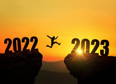 2023 uçurumundan atlayan adam inanılmaz bir günbatımında uçurumun üzerinden atlıyor. Yeni yıl konsepti. Mutlu yıllar 2023 'ün başlangıç ve hoşgeldin sembolü. İnsanlar 2023 yılına giriyor, yaratıcı fikir.
