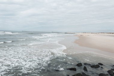 Okyanus kıyısındaki güzel kumlu sahil. Kayalar ve bulutlu gökyüzü.