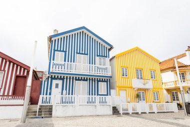 Portekiz 'in okyanus kıyısındaki bir balıkçı köyünde kapıları, pencereleri, terası, posta kutusu ve palmiyesi olan güzel çizgili sarı bir ev cephesi.