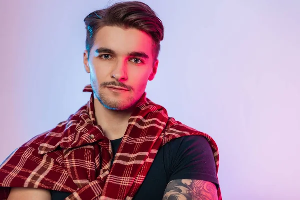Trendy fashionable male portrait of handsome hipster man hipster model with hairstyle, Mustache and beard in fashionable vintage outfit with plaid shirt in studio with colored creative pink lights