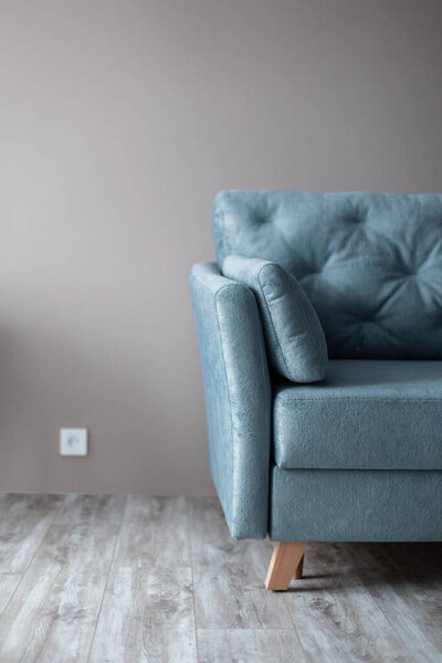 Удобный винтажный синий диван стоит рядом с бежевой стеной на деревянном полу. Внутри. Отдых дома