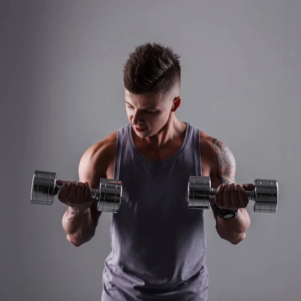 Strong powerful sporty man with muscular healthy body with metal dumbbells workout and trains in studio on a gray background