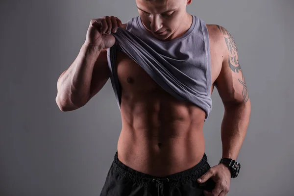 Handsome sexy muscular man with a muscular body takes off his shirt and shows off his abs muscle on a dark background in the studio. Health, Beauty and Diet