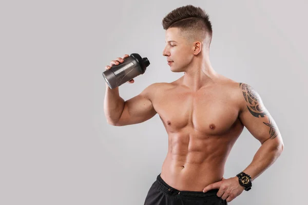 英俊的年轻男性运动员模型 头发和纹身都是光秃秃的肌肉躯干 从灰色背景的摇瓶中喝水 健康的生活方式 — 图库照片