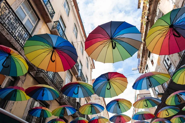 Brightly colored rainbow umbrellas in the air near a vintage building on the street. A creative colorful idea