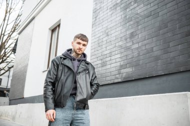 Moda giysileri içinde şık yakışıklı bir hippi. Siyah tuğlalı bir binanın yanında yürüyor.