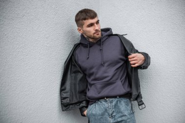 Şık giyinmiş, kapüşonlu, şık, yakışıklı bir hippi. Deri ceket giyiyor ve sokakta bir duvarın yanında duruyor.