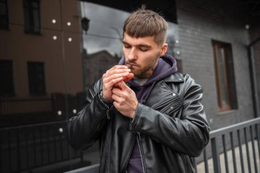 Havalı, modaya uygun, ceketli, kapüşonlu, havalı, vahşi hippi arka planda sigara içiyor.