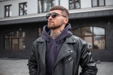 Şık, yakışıklı, hippi bir model. Şık bir kıyafet içinde, deri ceketli, kapüşonlu, güneş gözlüklü, sokakta yürüyor.