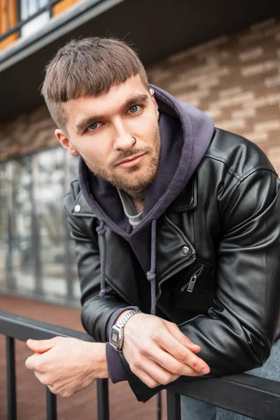 Elegante giovane uomo bello con un taglio di capelli corti in una moda nero  giacca invernale sorge sulla strada Foto stock - Alamy