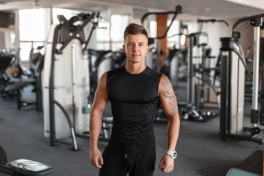 Yakışıklı, modaya uygun bir atletik erkek modelin portresi saç stili ve spor salonunun önünde tişörtlü siyah spor kıyafetli mükemmel kaslı bir vücut.