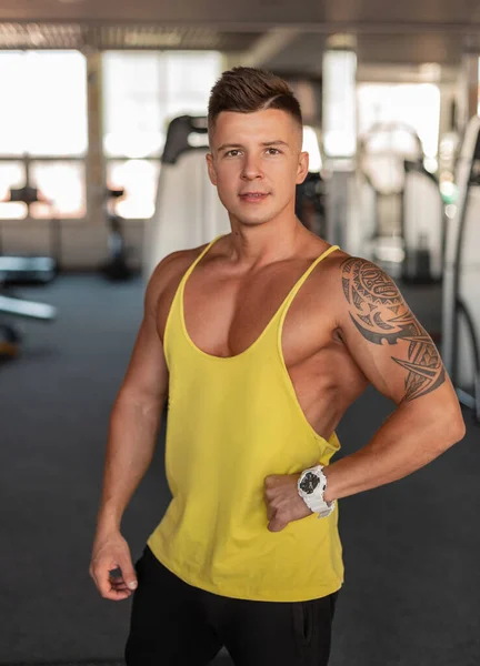Muscular handsome male model bodybuilder with an athletic body in a yellow tank top mockup in the gym