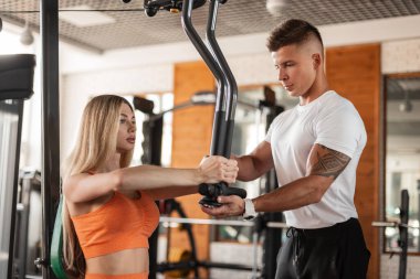 Beautiful blonde fitness woman with a man athlete partner work out together at the gym on a training apparatus