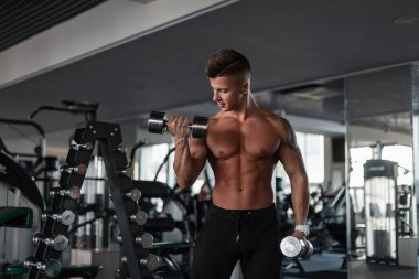 Atletik vücut kılı olan kaslı atletik yakışıklı adam spor salonunda dambıllarla egzersiz yapıyor.