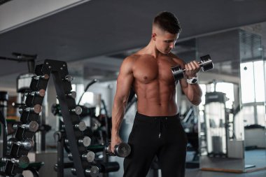 Sportif, yakışıklı vücut geliştiren, zayıf, sağlıklı vücut geliştiren, spor salonunda dambılları olan adam.