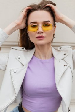 Sarı moda güneş gözlüklü, şık deri ceketli, şık bir kadın mankeni. Mor moda tişörtü sokakta poz veriyor.