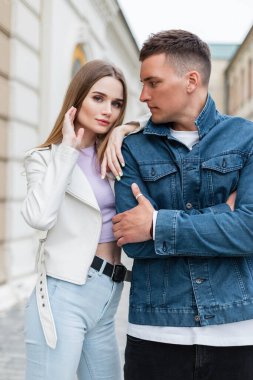 Havalı, şık, modaya uygun bahar kıyafetleri giymiş bir çift model sokakta yan yana poz veriyor. Güzel bir kadın ve kot ceketli şık bir hippi.