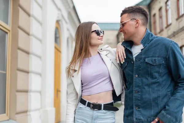 Stylish beautiful young couple with fashion sunglasses in fashionable denim casual clothes are walking in the city