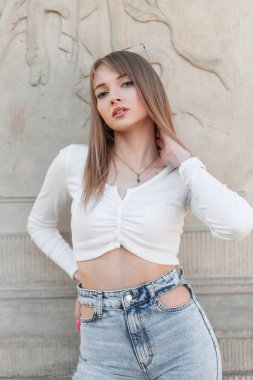 Fashionable young beautiful woman model in trendy stylish summer clothes with top and jeans on the street