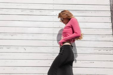 Şık güneş gözlüklü, uzun kollu, siyah etekli, şık, modaya uygun güneş gözlüklü güzel, seksi bir kız. Güneş ışığında beyaz, eski bir ahşap duvara yaslanmış.