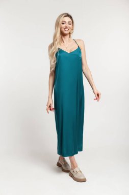 Şen sarışın, şık, şık, şık, şık elbiseli, ayakkabı standı olan güzel bir kadın. Stüdyoda beyaz arka planda poz veriyor.