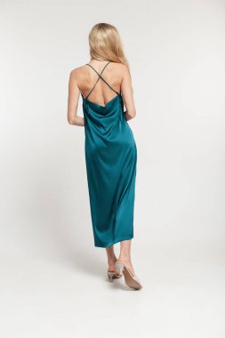 Moda modasında, şık, sarışın bir kadın. Arka askısı açık, ayakkabılı, beyaz bir arka planda duruyor.