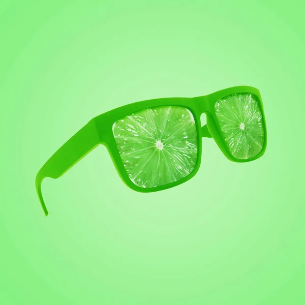 Fashion green sunglasses with juicy fresh lime floating on a green pastel background, creative idea. Vitamins, a concept.