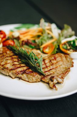 Beyaz tabakta marullu domuz bifteği siyah ahşap masada.