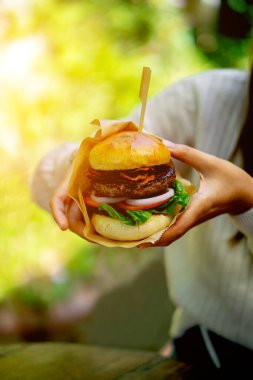Bir kadının iki elinde büyük bir hamburger..