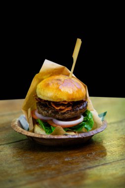 Büyük bir hamburger ahşap bir masaya ve siyah bir arka plana yerleştirilir..