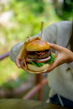 Bir kadının iki elinde büyük bir hamburger..