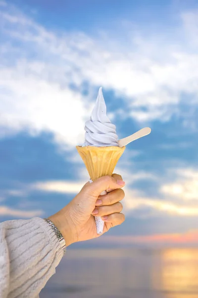 Hand holding soft ice cream against sky and sea backdrop