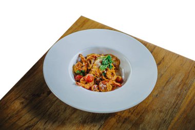 Beyaz bir zemin üzerinde ahşap bir masada büyük beyaz bir tabakta karides kremalı spagetti..