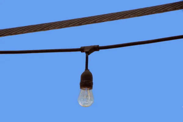 A single light bulb of an outdoor light chain seen against blue sky