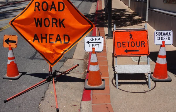 ROAD WORK, KEEP LEFT, DETOUR, SIDEWALK CLOSED signs on a city sidewalk construction site