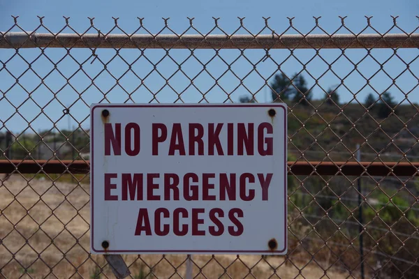 Sign on a fence at an industrial facility NO PARKING EMERGENCY ACCESS