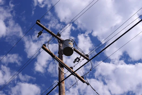 Electricity distribution pylon with transformers under blue sky with white clouds