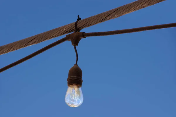 Single light bulb of an outdoor string light under blue sky