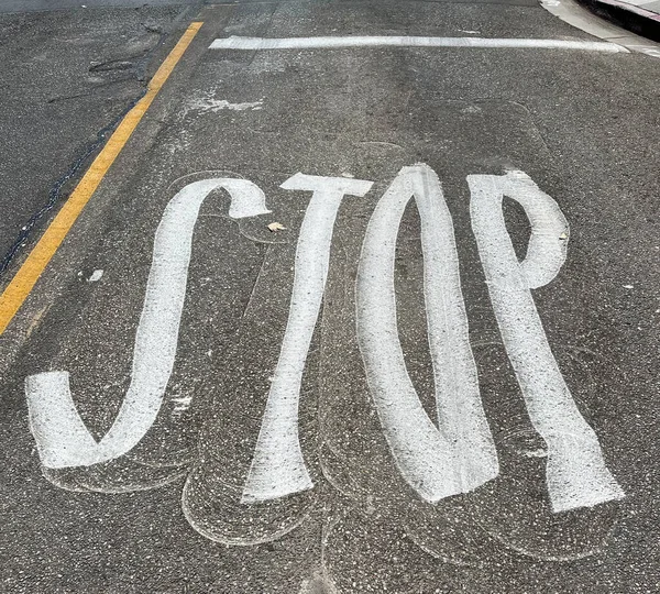 STOP signage on street asphalt before an intersection applied in a weird form