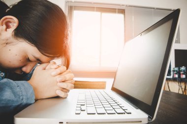 Kadın kız evde kalır ve diz üstü bilgisayarla Tanrı 'ya dua eder. Dua eden kızlar Coronavirus krizi için dua ederler. Ev kilisesi, çevrimiçi kilise, dua eden eller, evde ibadet