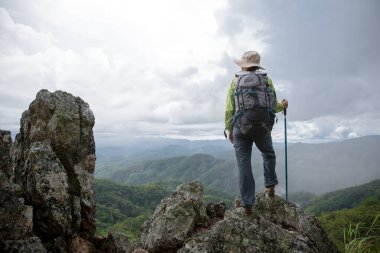 Sırt çantalı genç bir turist kayanın tepesinde dinleniyor ve dağların keyfini çıkarıyor.