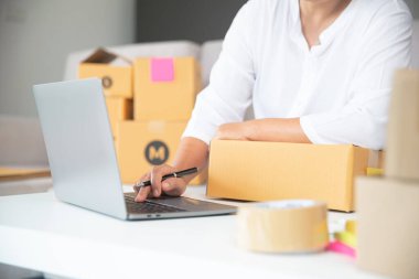 Kadın, ev ofisindeki klavye bilgisayarına bilgi yazarak müşterilerin ürünlerini sipariş ediyor.