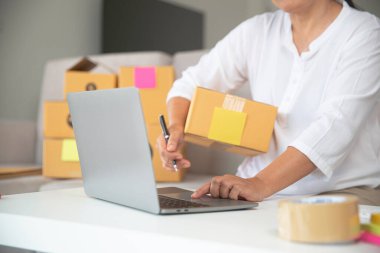 Kadın, ev ofisindeki klavye bilgisayarına bilgi yazarak müşterilerin ürünlerini sipariş ediyor.