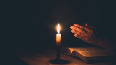 Kadın elleri kutsal İncil 'in üzerine dua ediyor. Mumlar seçilmiş odak noktasında. Güzel altın arka plan. Din kavramı.
