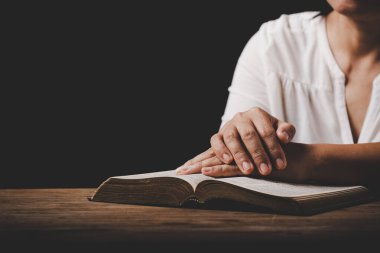 Close up of christian woman hand on holy bible are pray and worship for thank god in church with black background, adult female person are reading book, concept for faith, spirituality and religion