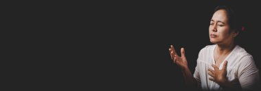 Asyalı Hristiyan kadın kilisede dua eder ve ibadet eder siyah arka planlı Tanrı 'ya inanç, maneviyat ve din kavramı, yatay bayrak.