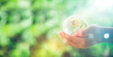 Human hands holding earth sphere crystal or sustainable globe glass with sunlight at green nature background in ecology environment forest. concept of conservation environmental, protection planet.